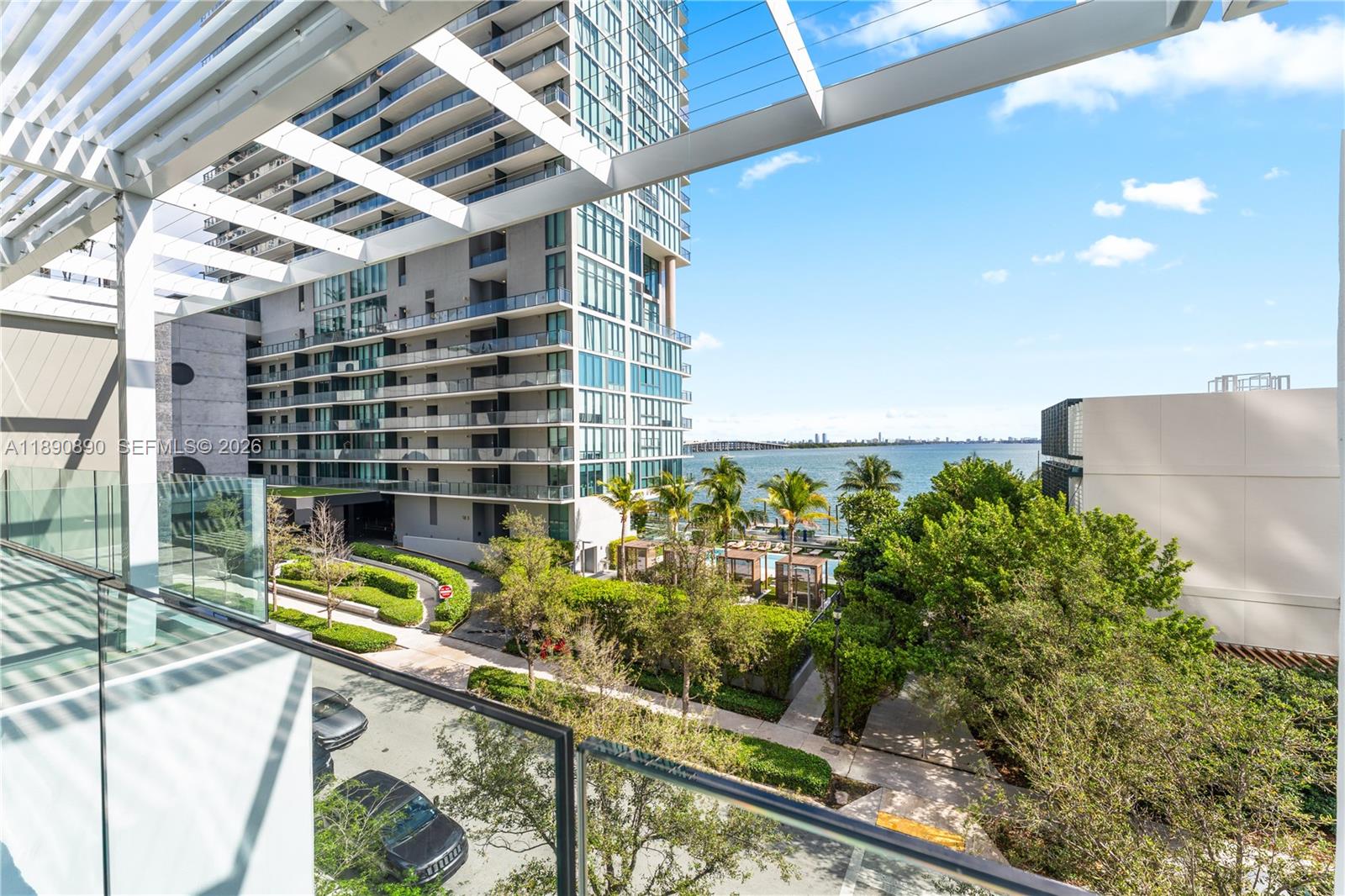 A balcony view overlooks a modern high-rise building, lush landscaping, and a waterfront bay — 650 NE 32nd St, Miami FL 33137, MIAMI, FL