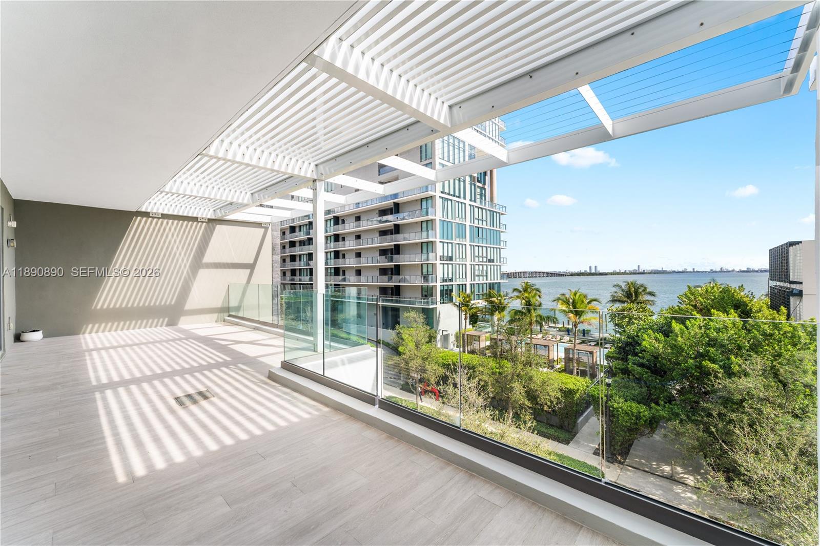 A spacious balcony features light wood-look flooring, a white slatted pergola, and glass railings — 650 NE 32nd St, Miami FL 33137, MIAMI, FL