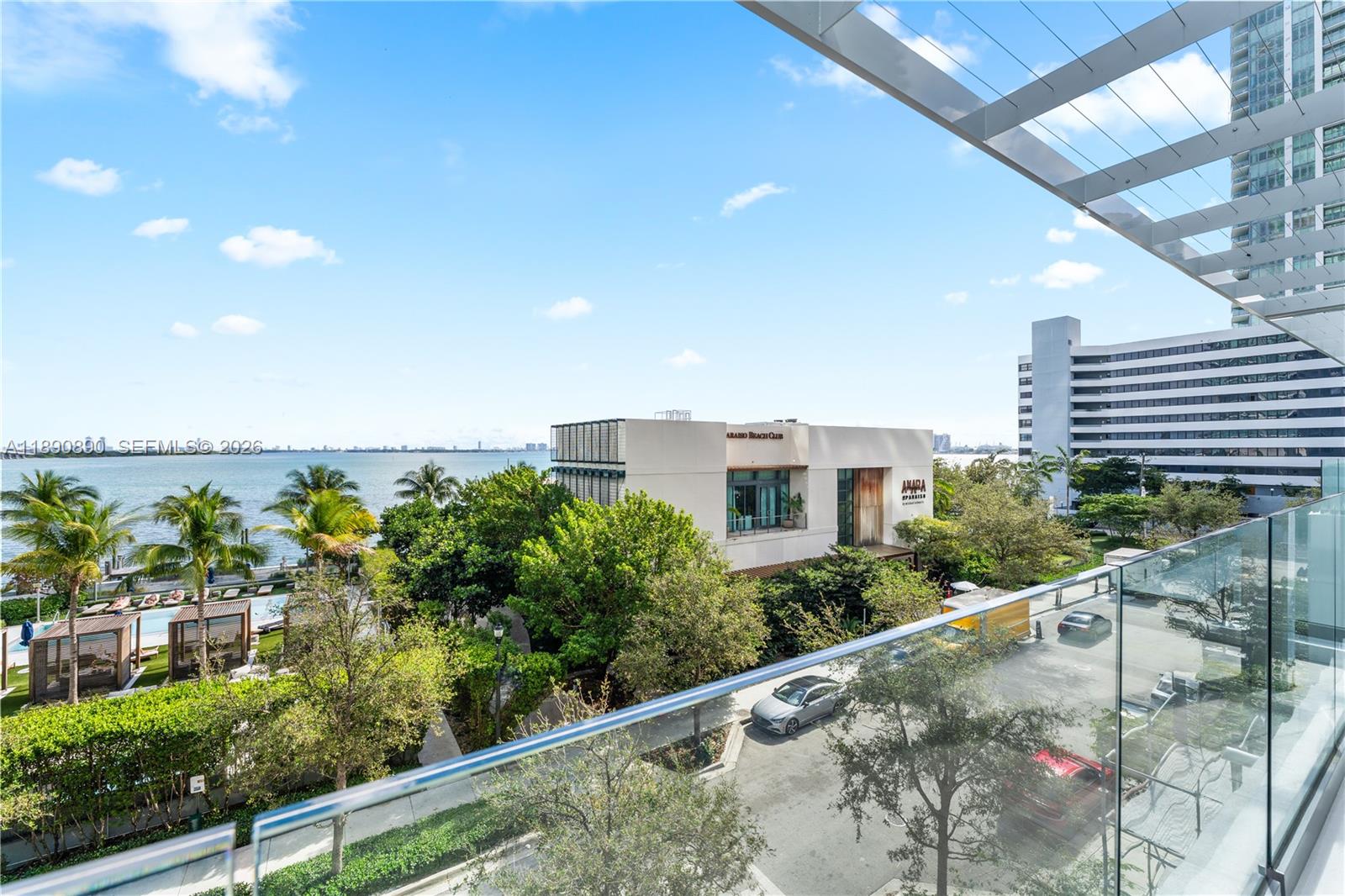 A balcony view overlooks a waterfront restaurant, lush trees, and a parking area — 650 NE 32nd St, Miami FL 33137, MIAMI, FL