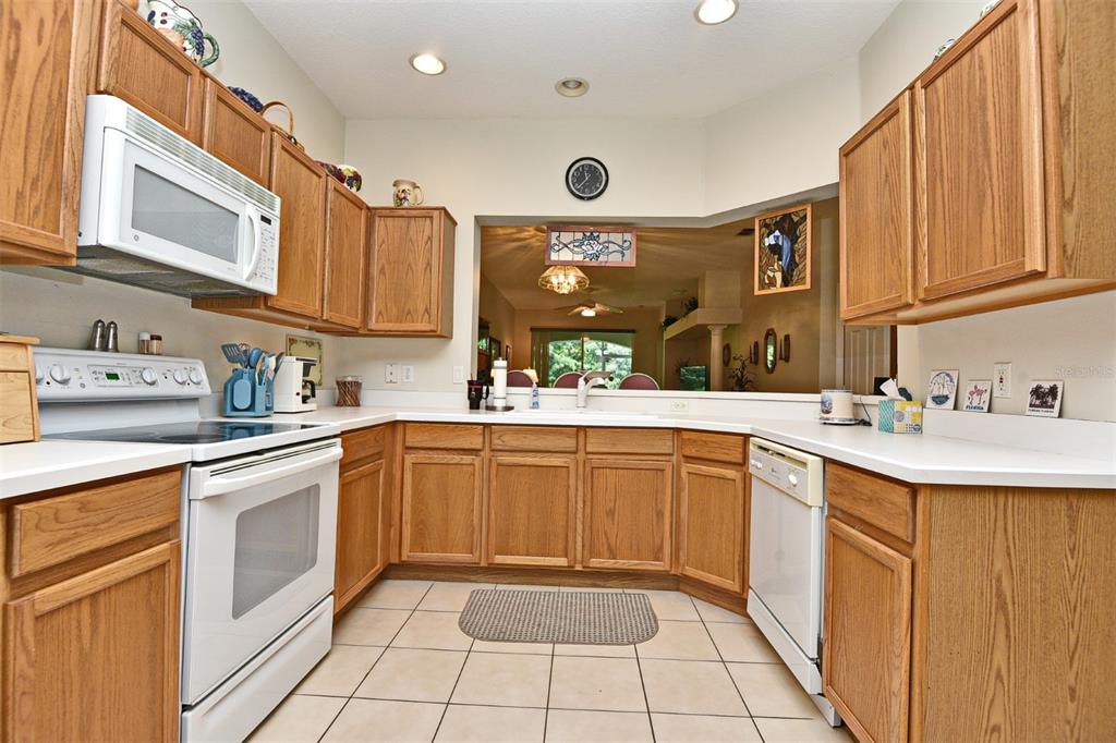 A kitchen with oak cabinets, white appliances, a pass-through window, and light-colored tile flooring — 3132 RIVER BRANCH CIRCLE, KISSIMMEE, FL