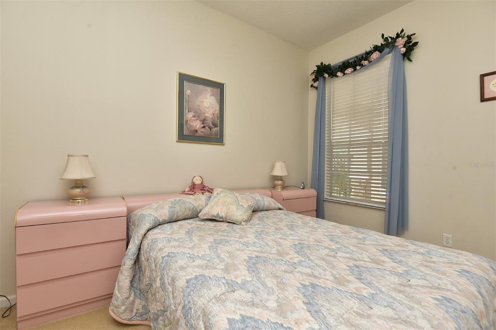 A bedroom features a bed with a patterned quilt, pink nightstands, and blue window curtains — 3132 RIVER BRANCH CIRCLE, KISSIMMEE, FL