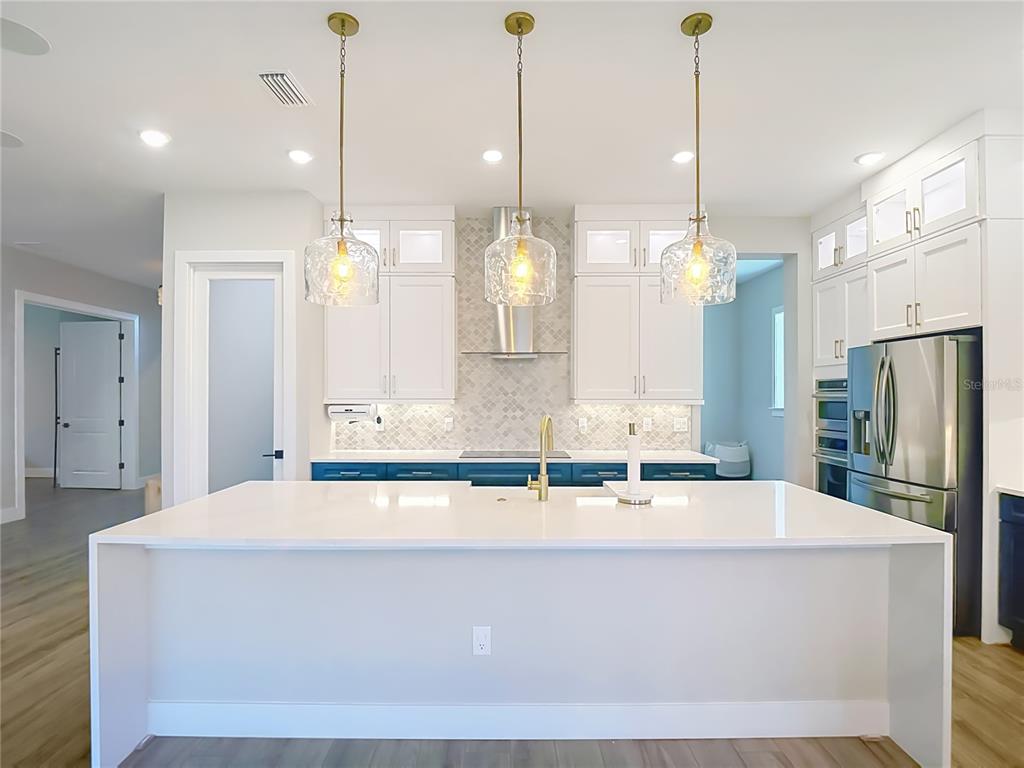 A modern kitchen features a large white island, blue lower cabinets, and three glass pendants — 8891 DRUMMER PLANK DRIVE, WESLEY CHAPEL, FL