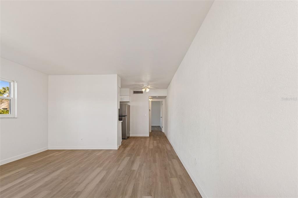 A bright, empty living room with light wood-look flooring and a view into the kitchen — 4565 DUHME ROAD UNIT 101, ST PETERSBURG, FL