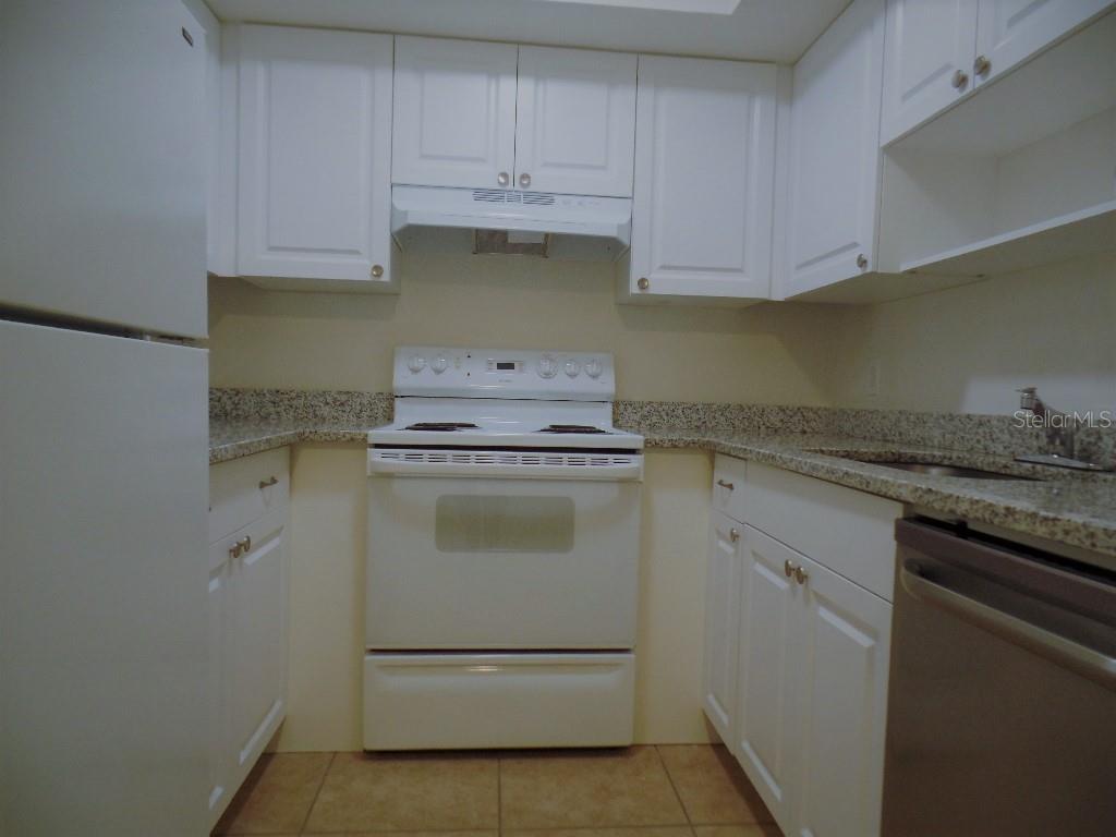 A galley kitchen features white cabinets, granite countertops, and white appliances — 1240 70TH STREET N UNIT 7, ST PETERSBURG, FL