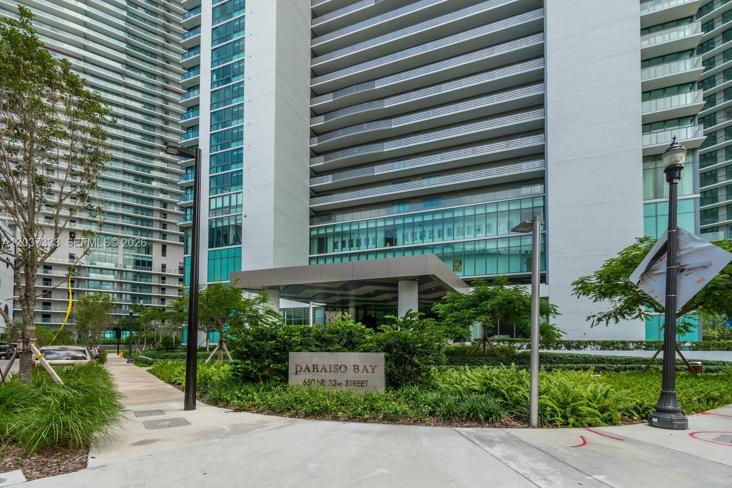 The exterior of a modern high-rise residential building features a stone entrance sign and landscaping — 650 NE 32nd St # 805, Miami FL 33137, MIAMI, FL