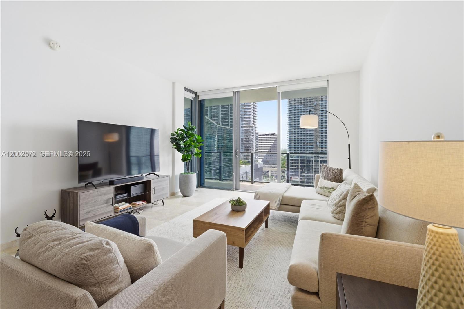 A modern living room features a sectional sofa, television console, and floor-to-ceiling balcony windows — 68 SE 6th St # 1106, Miami FL 33131, MIAMI, FL