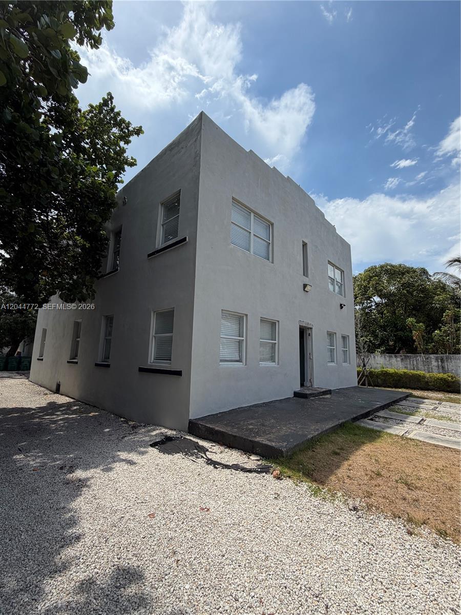 A two-story, light-gray stucco building stands next to a gravel driveway under a blue sky — 6828 NW 3rd Ave # 2, Miami FL 33150, MIAMI, FL