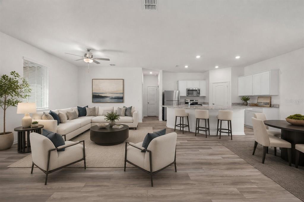 An open-concept living room and kitchen featuring light wood floors, white cabinetry, and neutral furniture — 357 BREAM, POINCIANA, FL