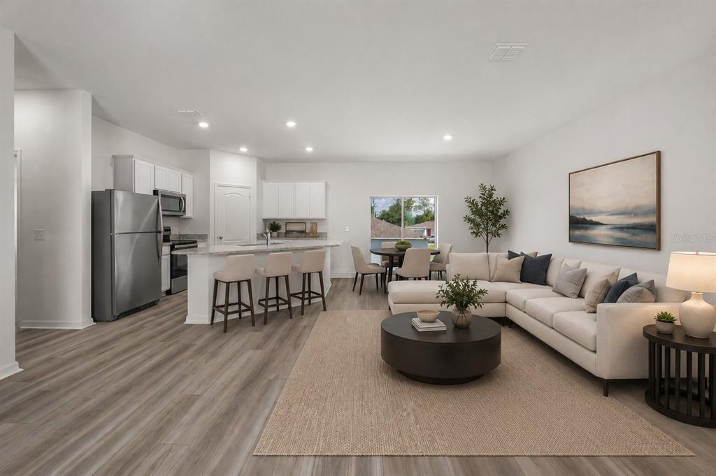An open-concept living room and kitchen featuring light wood flooring, white cabinetry, and neutral furniture — 357 BREAM, POINCIANA, FL
