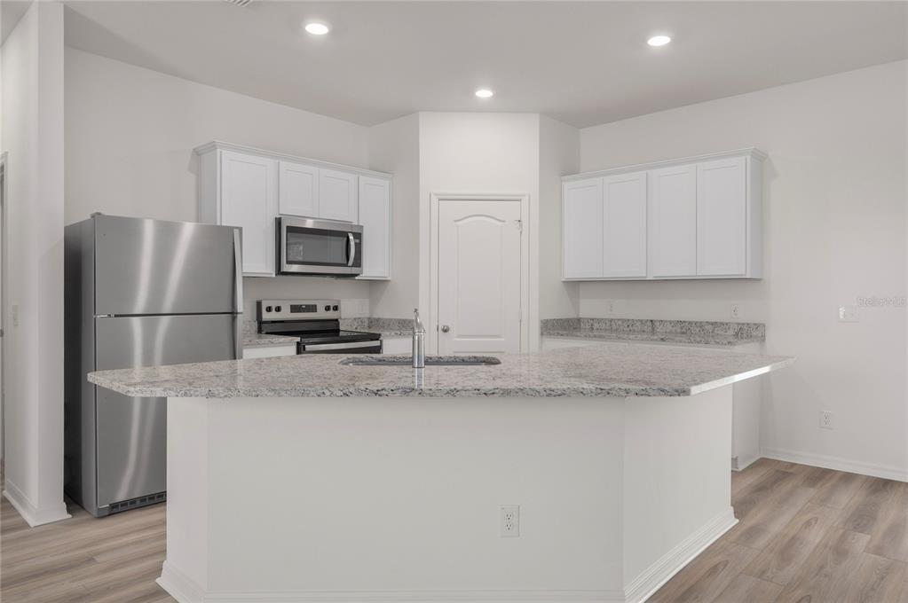 A kitchen features white cabinets, stainless steel appliances, and a granite-topped island with a sink — 357 BREAM, POINCIANA, FL