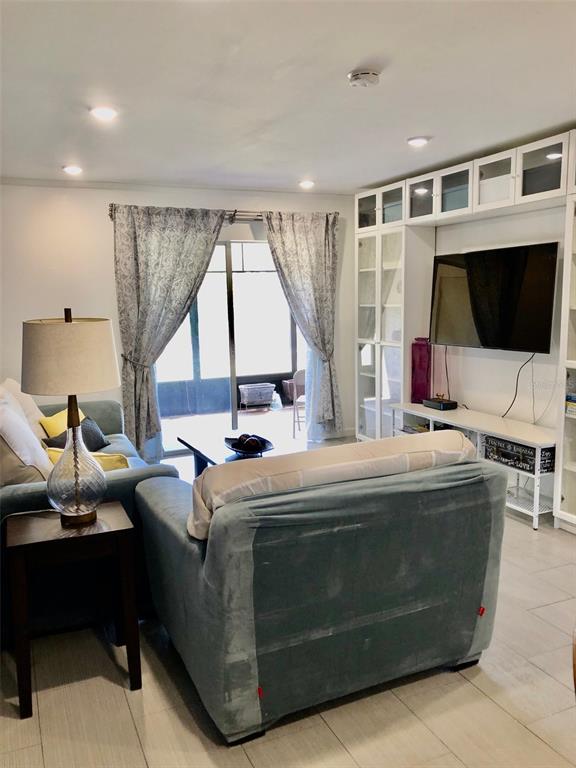 A living room features a blue sofa, a television on a wall unit, and curtains — 102 CAPRI ISLES BOULEVARD UNIT 106, VENICE, FL