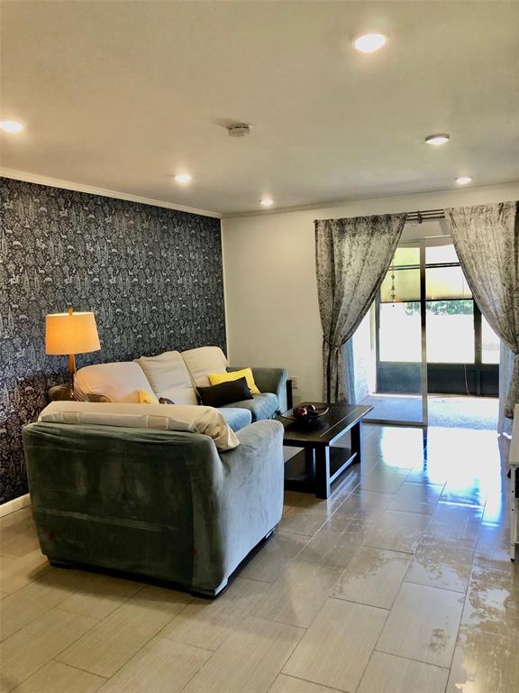 A living room features a patterned accent wall, a gray sofa, and tiled flooring — 102 CAPRI ISLES BOULEVARD UNIT 106, VENICE, FL