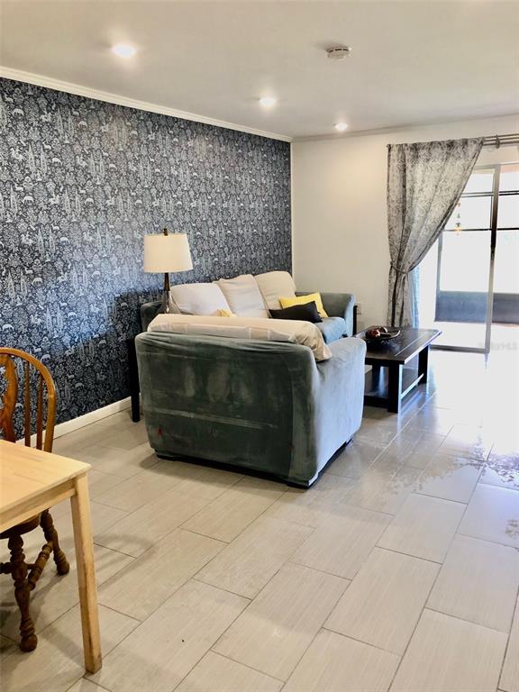 A living room features a patterned accent wall, a gray sofa, and light tile flooring — 102 CAPRI ISLES BOULEVARD UNIT 106, VENICE, FL