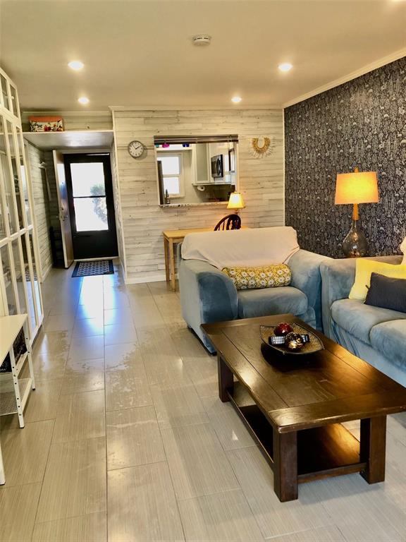 A living room with light tile floors, a dark wood coffee table, and patterned wallpaper — 102 CAPRI ISLES BOULEVARD UNIT 106, VENICE, FL