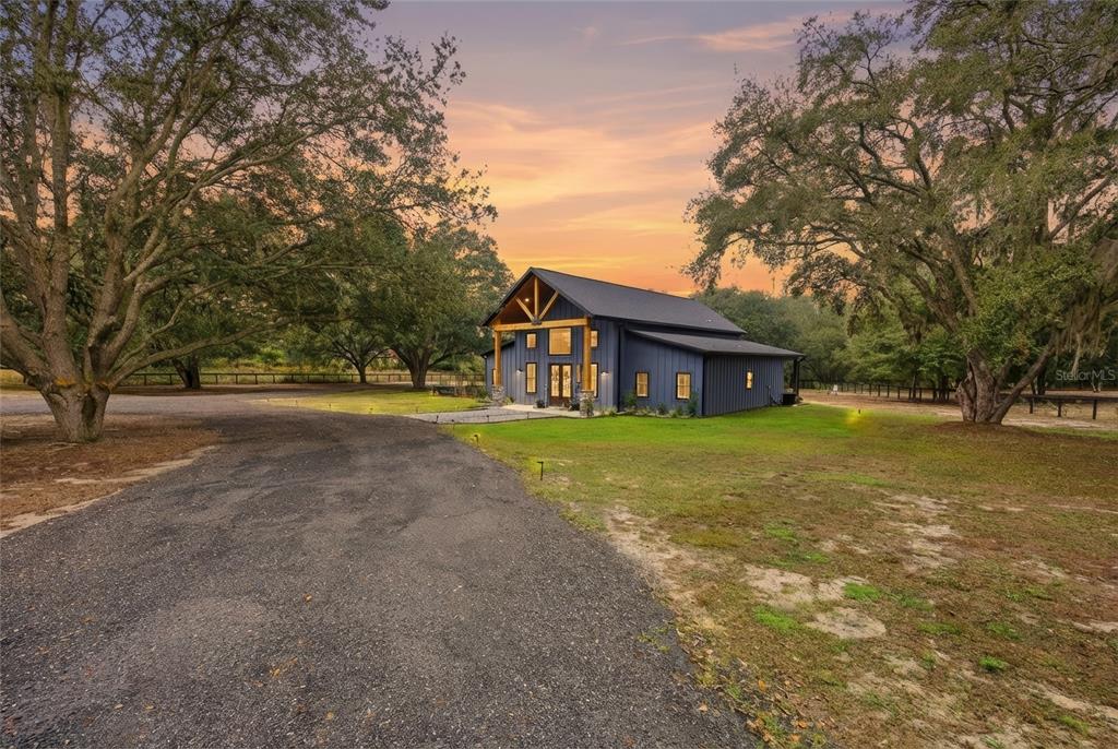 A dark blue modern farmhouse with a wooden porch frame sits on a grassy lot — 12052 SE 101ST COURT ROAD, BELLEVIEW, FL