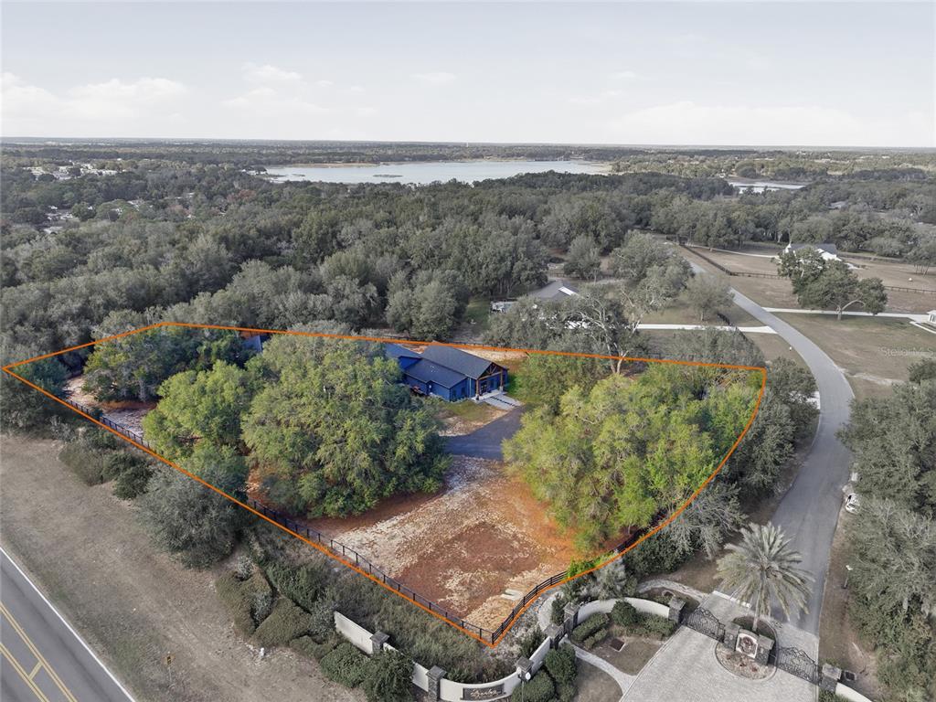 An aerial view shows a dark blue house situated on a wooded, fenced lot — 12052 SE 101ST COURT ROAD, BELLEVIEW, FL