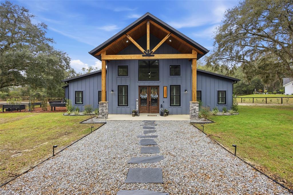 A blue modern farmhouse with a large timber-framed porch and a gravel walkway — 12052 SE 101ST COURT ROAD, BELLEVIEW, FL