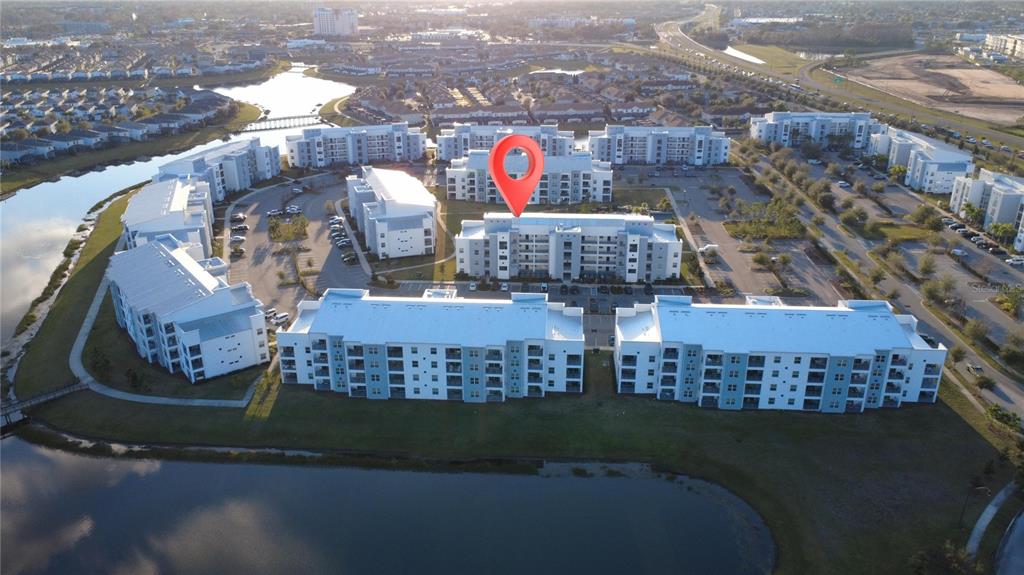 An aerial view of a multi-story apartment complex situated next to a pond — 3180 PARADOX CIRCLE UNIT 102, KISSIMMEE, FL