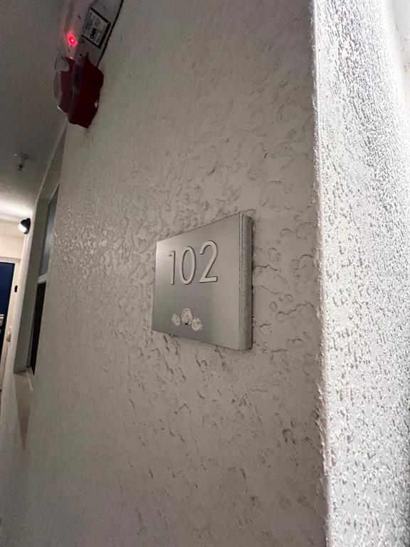 A silver sign with the number 102 is mounted on a textured white wall — 3180 PARADOX CIRCLE UNIT 102, KISSIMMEE, FL