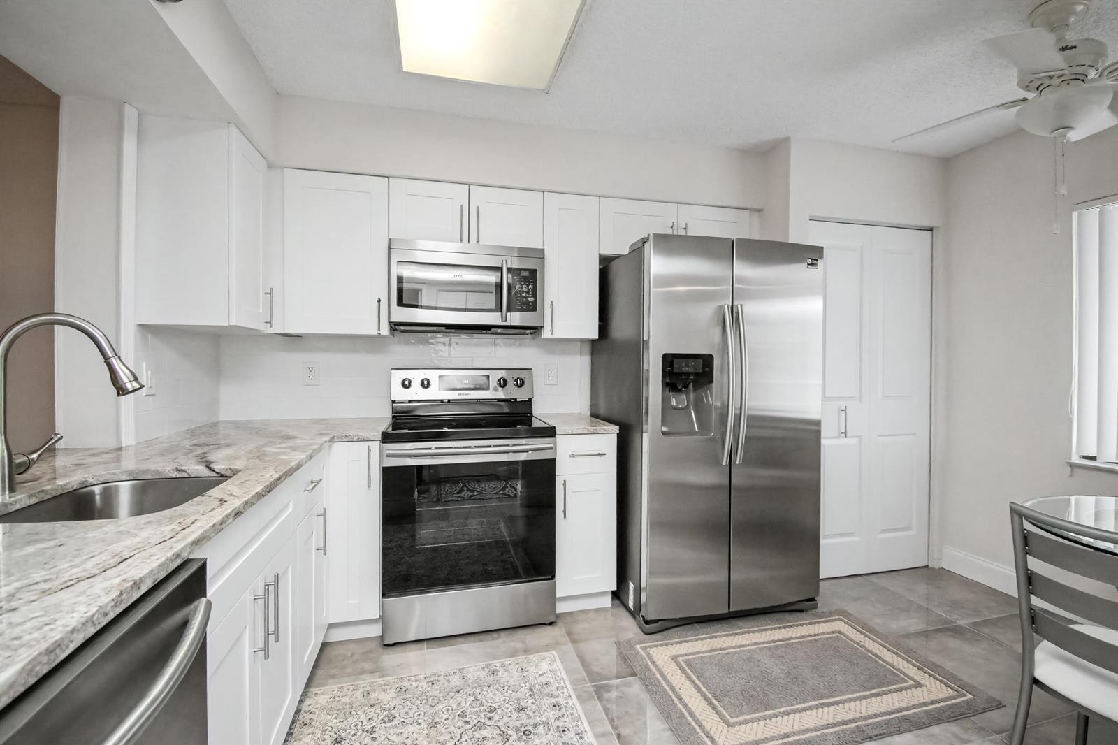 A kitchen features white cabinets, stainless steel appliances, and granite countertops — 7351 Kinghurst Drive # 301, Delray Beach FL 33446, DELRAY BEACH, FL