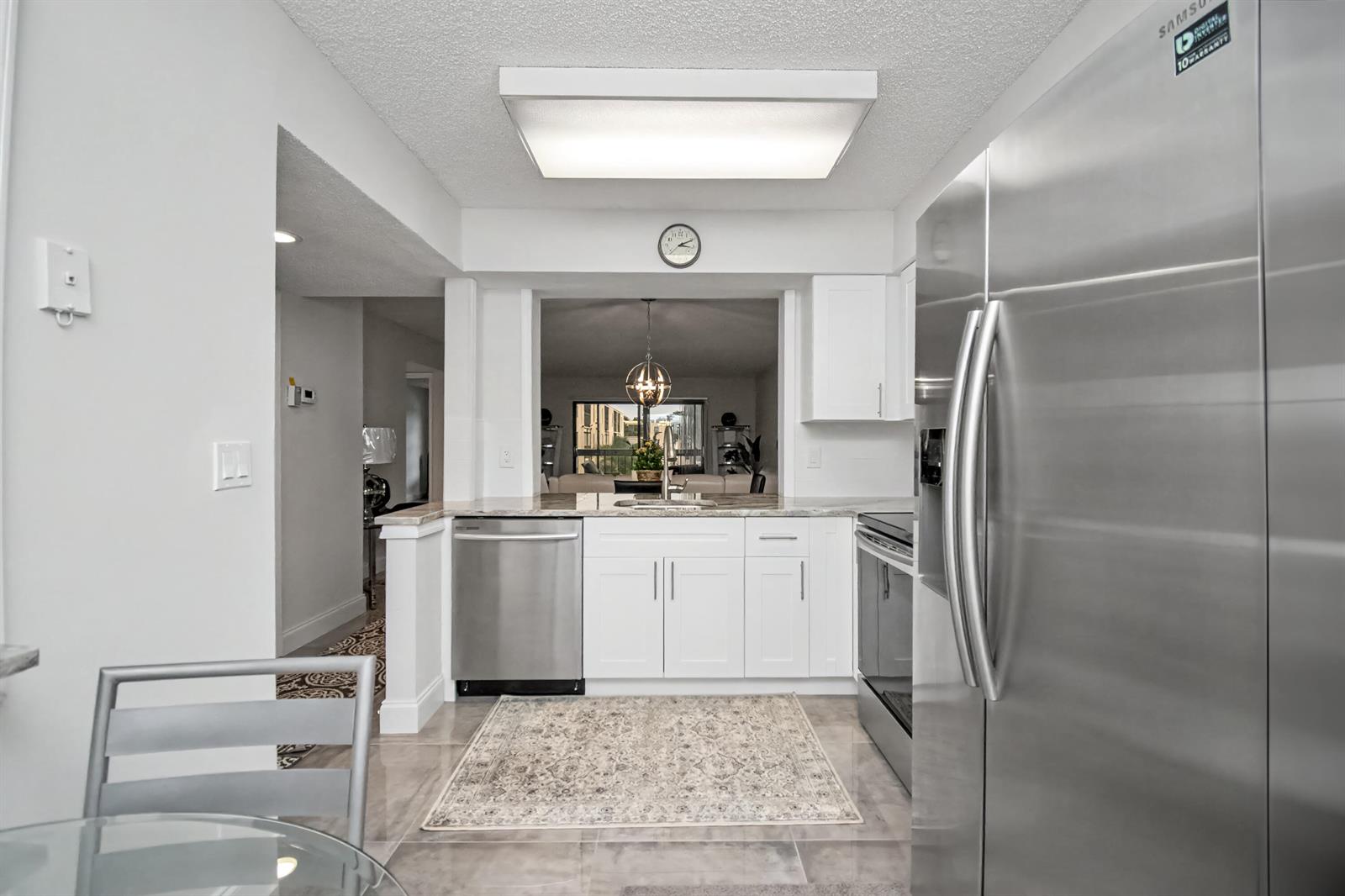 A kitchen features white cabinets, stainless steel appliances, and a pass-through window to the living area — 7351 Kinghurst Drive # 301, Delray Beach FL 33446, DELRAY BEACH, FL