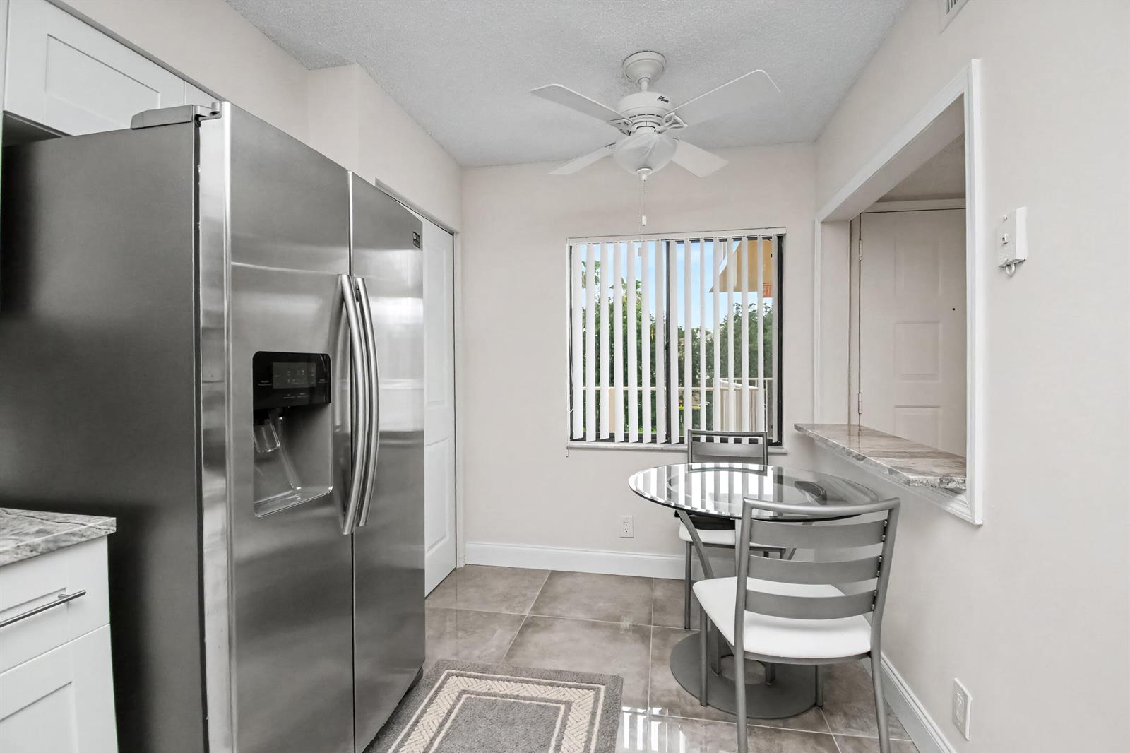 A kitchen dining area features a stainless steel refrigerator, tile flooring, and a glass table — 7351 Kinghurst Drive # 301, Delray Beach FL 33446, DELRAY BEACH, FL