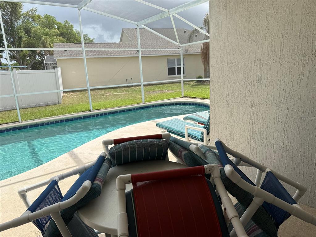A covered patio overlooks a swimming pool enclosed by a screen cage — 1122 CLEAR CREEK CIRCLE, CLERMONT, FL