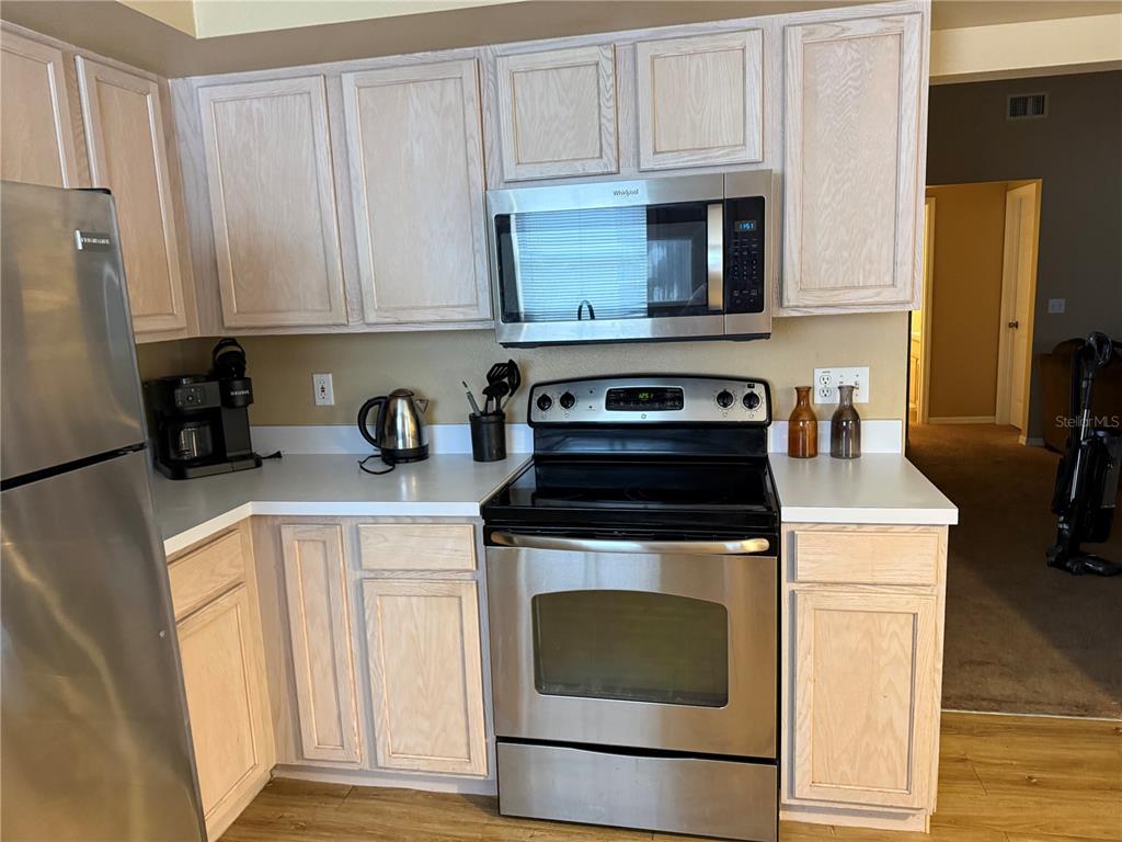 A kitchen features light wood cabinets, stainless steel appliances, and white countertops — 1122 CLEAR CREEK CIRCLE, CLERMONT, FL