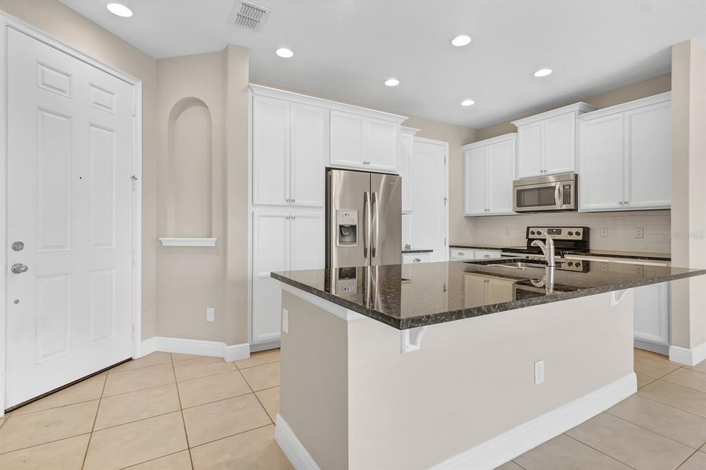 A kitchen with white cabinets, stainless steel appliances, a dark granite island, and tile flooring — 14481 SWANLEY STREET, ORLANDO, FL