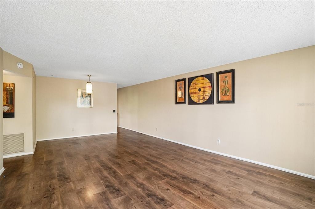 An empty living room features light beige walls, wood-look flooring, and decorative wall art — 2402 ECUADORIAN WAY UNIT 28, CLEARWATER, FL