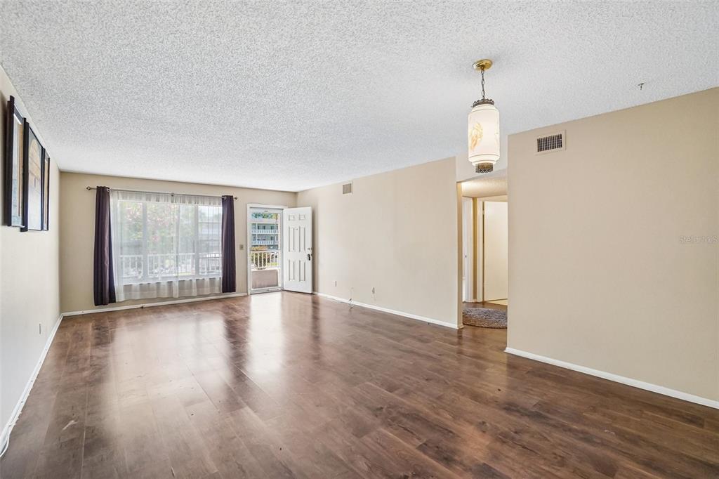 An empty living room features wood-look flooring, beige walls, a textured ceiling, and a pendant light — 2402 ECUADORIAN WAY UNIT 28, CLEARWATER, FL