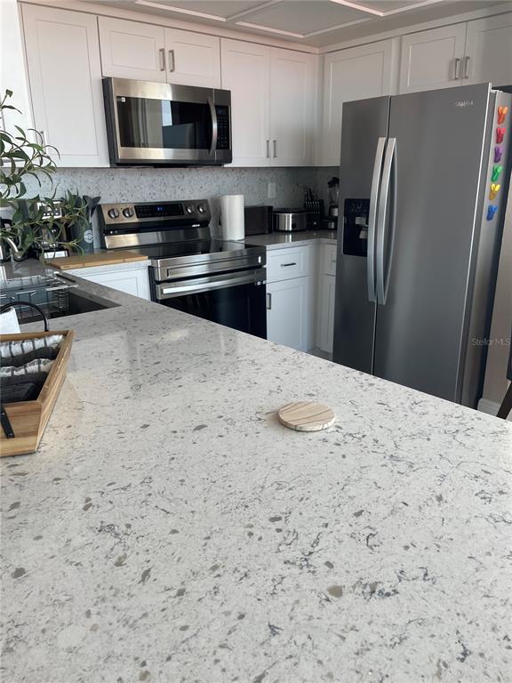 A kitchen features white cabinets, stainless steel appliances, and a large speckled quartz countertop — 6211 SUN BOULEVARD UNIT 306, ST PETERSBURG, FL