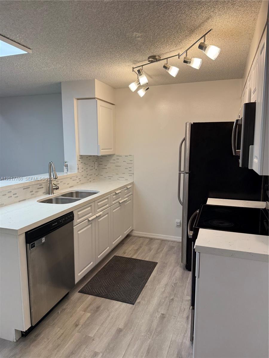 A kitchen features white cabinets, stainless steel appliances, light countertops, and wood-look flooring — WESTON, FL