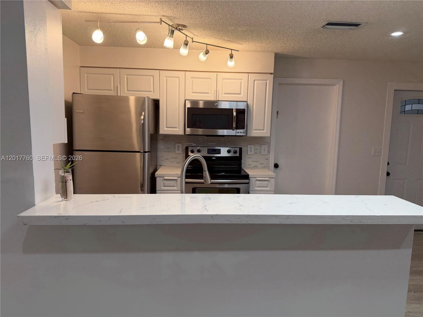 A kitchen features white cabinets, stainless steel appliances, and a white marble-look countertop island — WESTON, FL