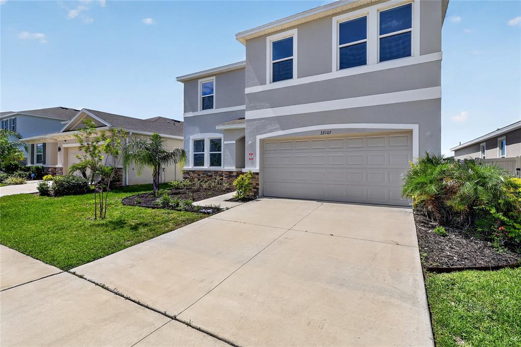 A two-story suburban house features a gray exterior, a two-car garage, and a concrete driveway — 32107 CONCHSHELL SAIL STREET, WESLEY CHAPEL, FL