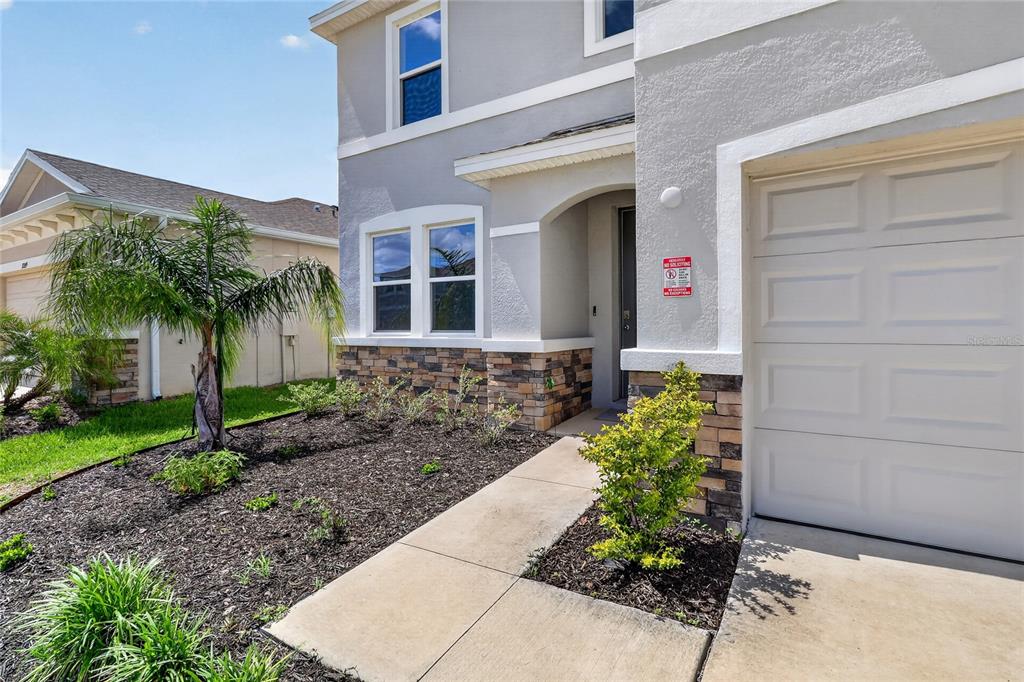 A two-story house exterior features a stone-accented facade, a concrete walkway, and a garage — 32107 CONCHSHELL SAIL STREET, WESLEY CHAPEL, FL