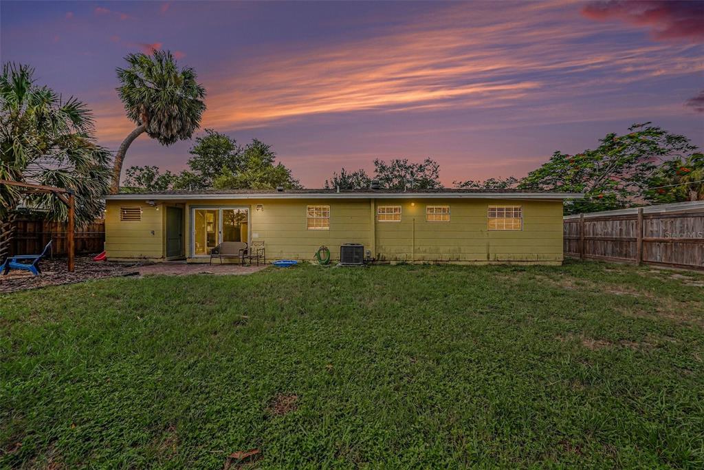 The exterior rear view of a single-story house with yellow siding and a grassy yard — 4733 W WISCONSIN AVENUE, TAMPA, FL