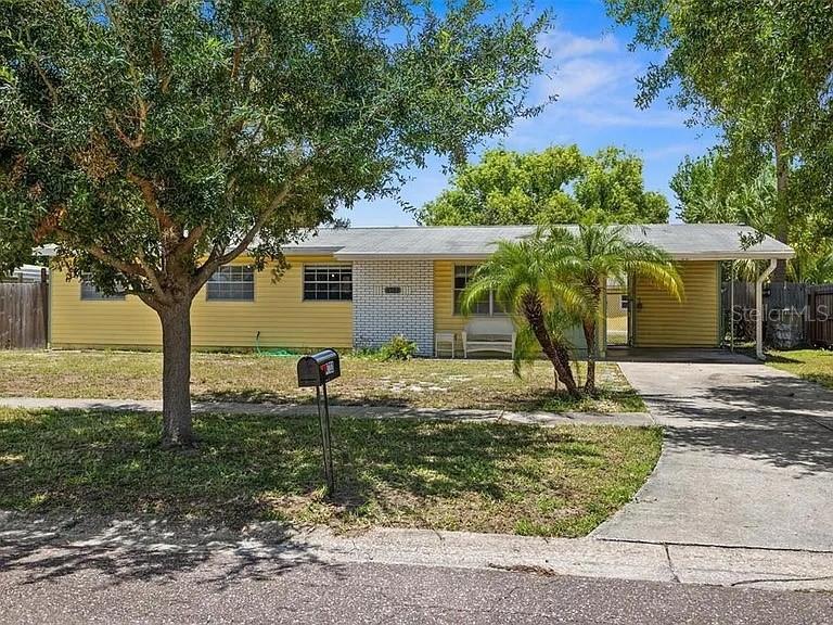 A single-story yellow house with a brick facade, a carport, and a front lawn — 4733 W WISCONSIN AVENUE, TAMPA, FL