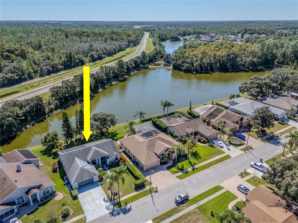 An aerial view shows a suburban house with a pool cage near a lake — 4938 YELLOWSTONE DRIVE, NEW PORT RICHEY, FL