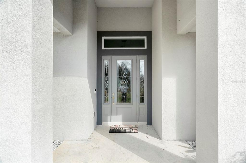 A gray front door with glass panels and a transom window sits under a covered entryway — 3038 VELVET LANE, NORTH PORT, FL