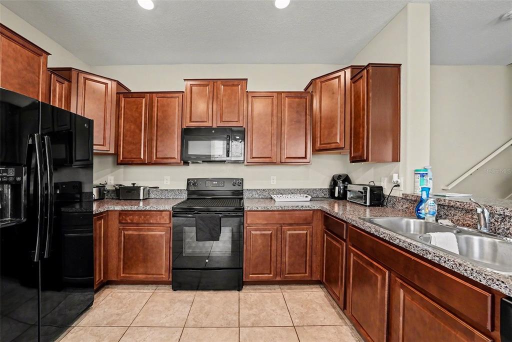 A kitchen with wood cabinets, black appliances, and granite countertops — 7655 GINGER LILY COURT, TAMPA, FL