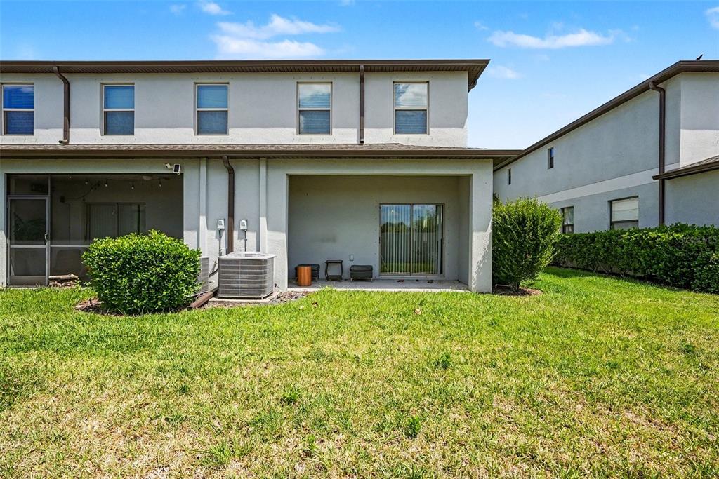 The exterior of a two-story townhouse features a covered patio, a lawn, and an AC unit — 7655 GINGER LILY COURT, TAMPA, FL