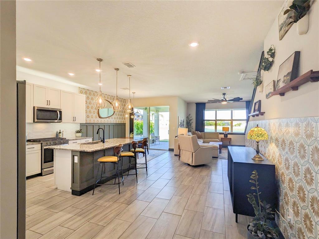 An open-concept kitchen and living area features a large island, tile flooring, and patterned wallpaper — 3324 BIG SKY WAY, LAKEWOOD RANCH, FL
