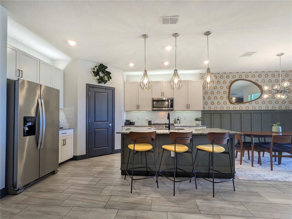 A modern kitchen features a central island with three yellow stools and pendant lighting — 3324 BIG SKY WAY, LAKEWOOD RANCH, FL