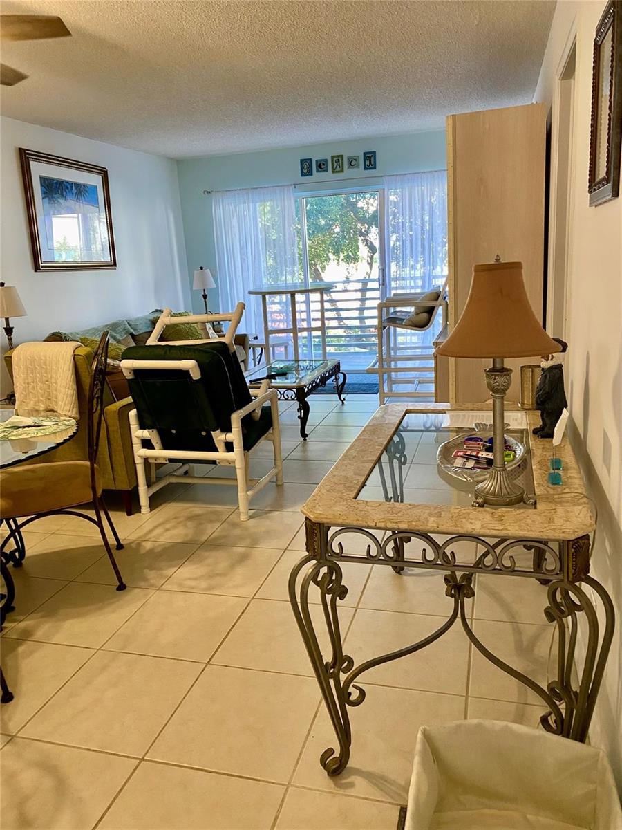 A living room features tile flooring, a glass-topped console table, and a sliding glass balcony door — 1541 S Ocean Boulevard # 324, Pompano Beach FL 33062, POMPANO BEACH, FL