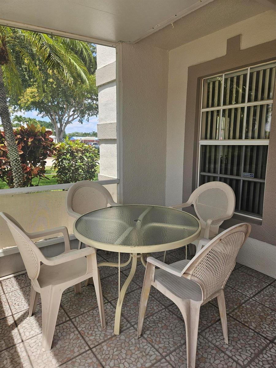 A glass-topped patio table with four plastic chairs sits on a tiled screened-in porch — 18999 Stewart Circle # 8, Boca Raton FL 33496, BOCA RATON, FL
