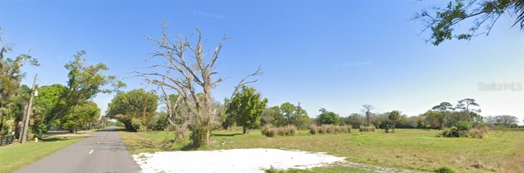A paved road runs alongside a large, open grassy lot with scattered trees and vegetation — 1376 NE 48TH AVENUE, OKEECHOBEE, FL