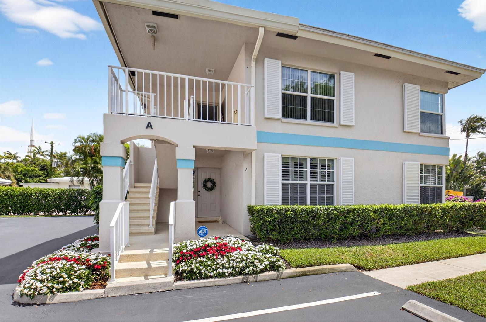 A two-story apartment building exterior features a white staircase, a balcony, and landscaped flower beds — 75 Venetian Drive # 2, Delray Beach FL 33483, DELRAY BEACH, FL