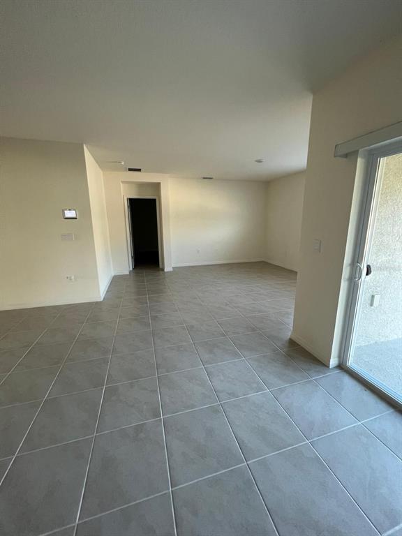 An open-concept living area features light-colored tile flooring, beige walls, and a sliding glass door — 2710 TRINIDAD ROAD, HAINES CITY, FL
