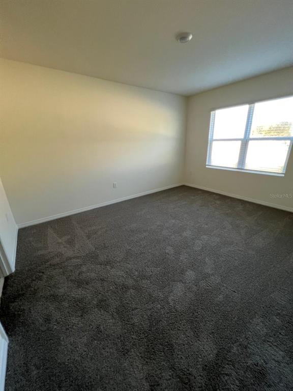 An empty bedroom features beige walls, dark gray carpeting, and a single window — 2710 TRINIDAD ROAD, HAINES CITY, FL